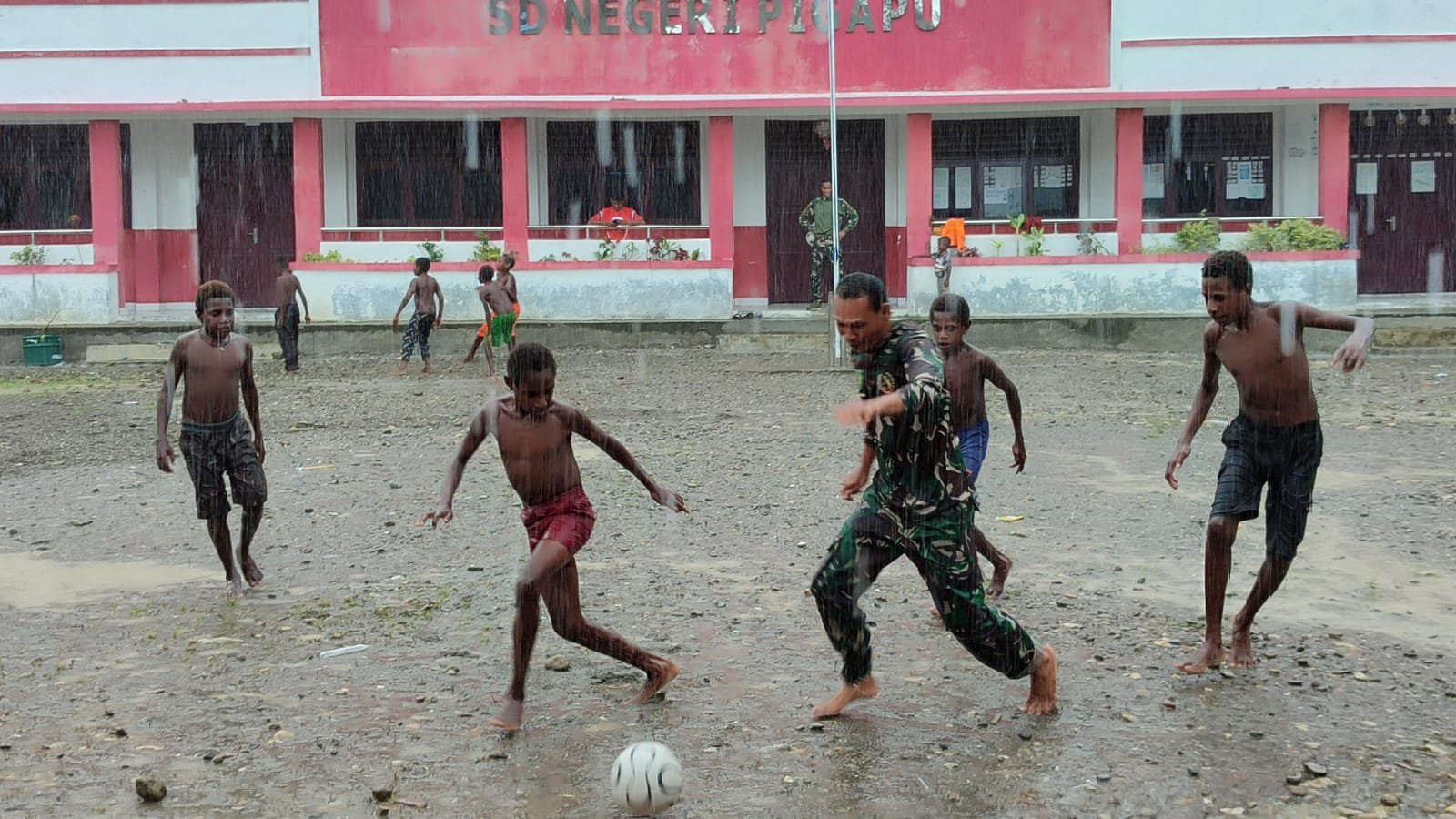 Personel Satgas TMMD Bermain Sepak Bola Bersama Anak-anak Meski Diguyur Hujan