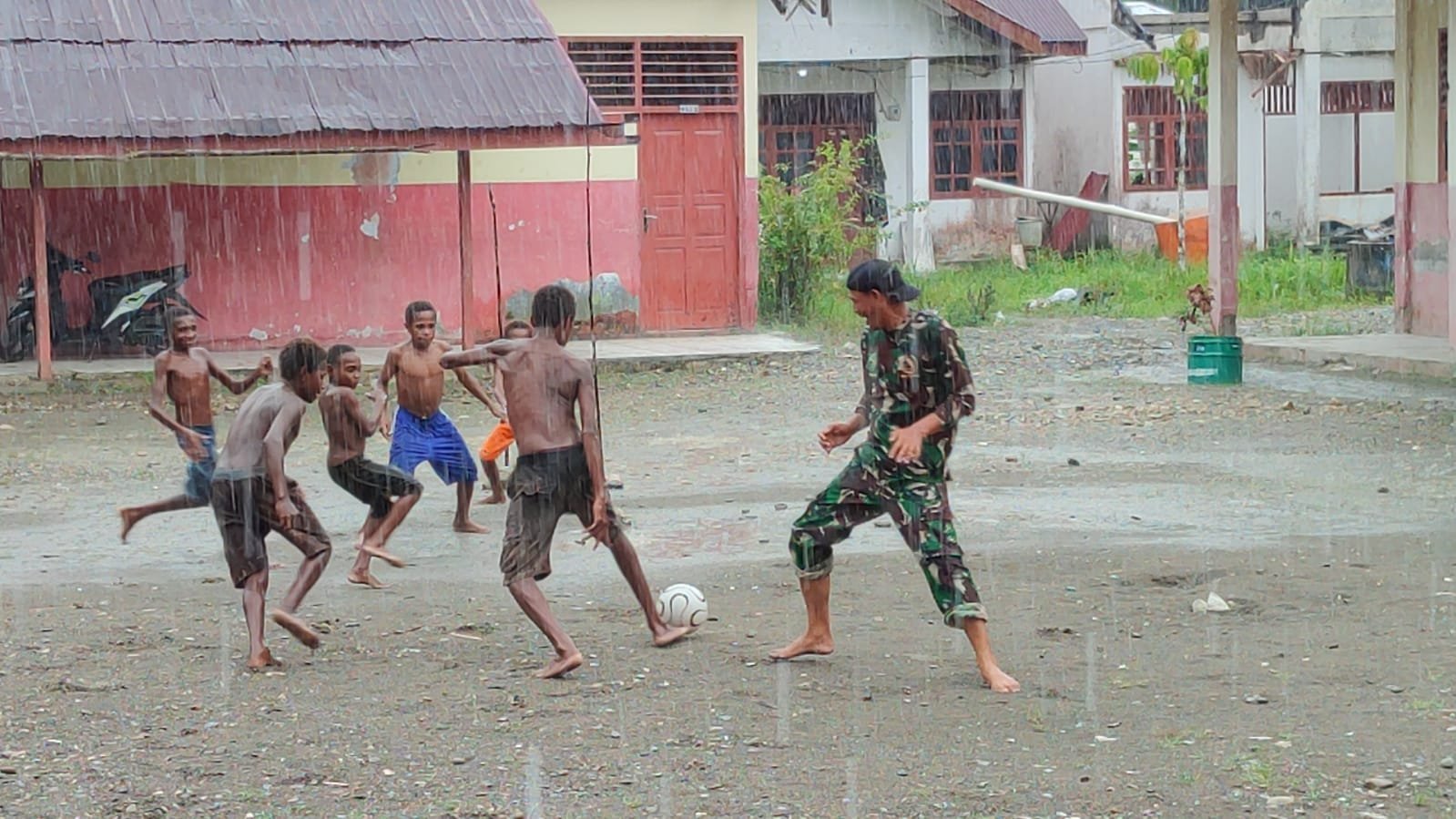 Personel Satgas TMMD Bermain Sepak Bola Bersama Anak-anak Meski Diguyur Hujan